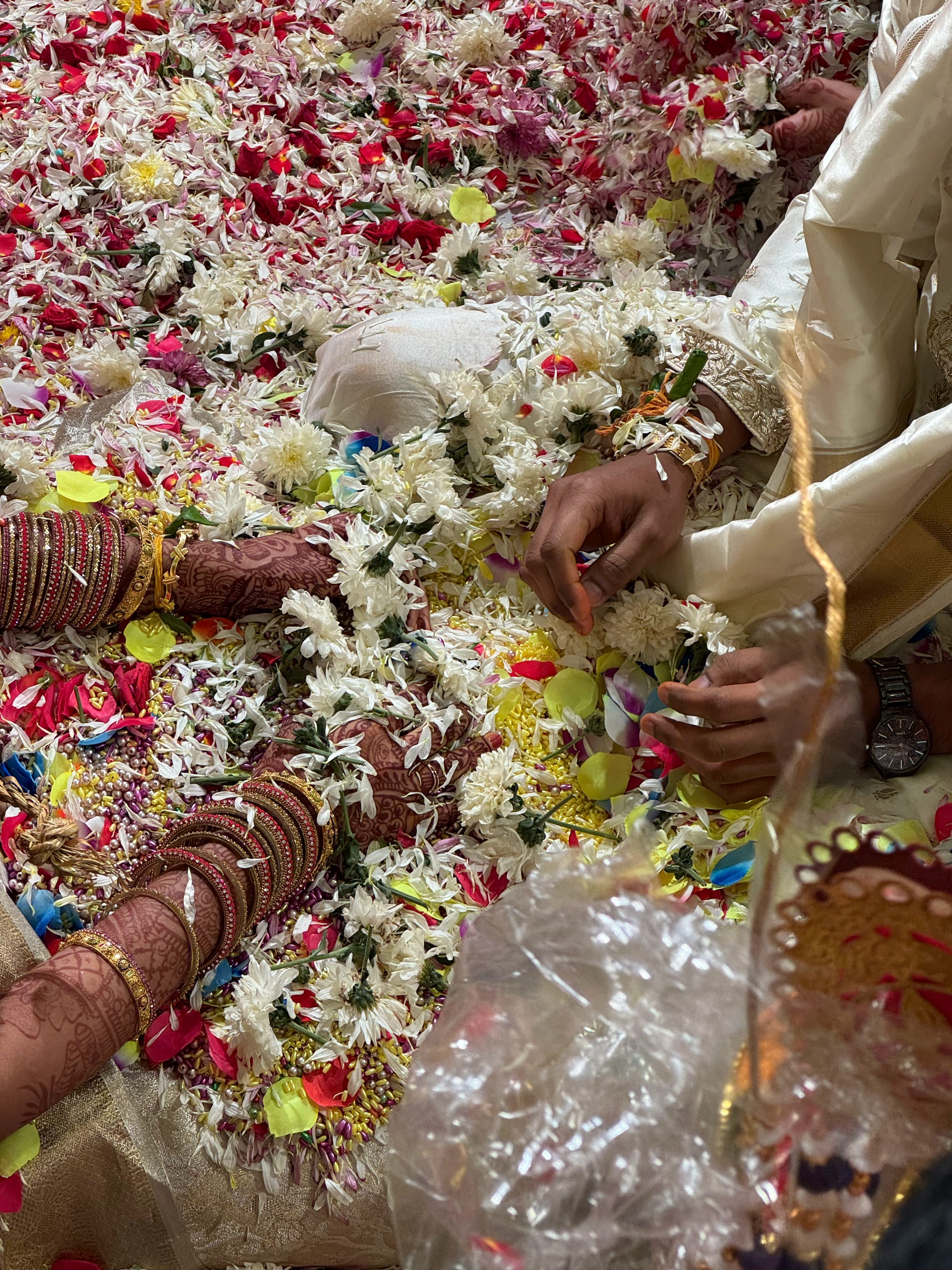 Hands decorated with henna and bangles surrounded by flower petals at an Indian wedding ceremony